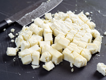 Photo of freshly cut Paneer cheese on a cutting board with knife in the background. Shallow focus across the middle.の写真素材