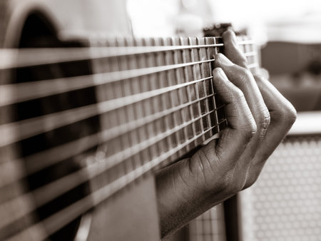 Closeup photo of a man playing his acoustic guitar. Focus on the fingers.