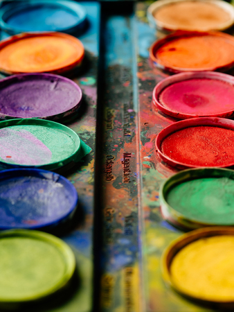 Photo of a palette of watercolor paints on a well-used tray.の写真素材