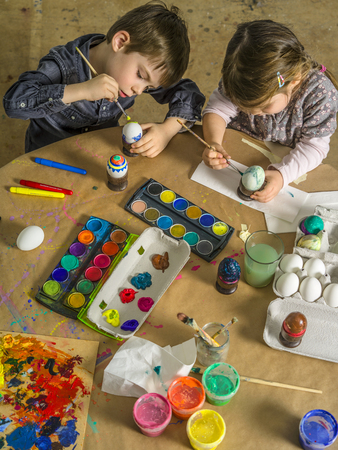 Photo of a brother and sister painting and decorating hard-boiled eggs for easter.の写真素材