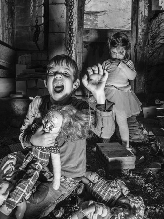 Photo of creepy young children standing over old dolls and in a barn covered in spiderwebs and dust.の写真素材