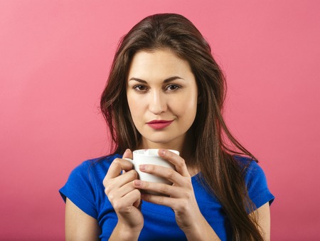 Photo of a gorgeous young woman drinking coffee over a pink background.の写真素材