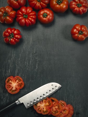 Photo of a table top with Marmande tomatoes, a knife, and slices with copy space in the middle.の写真素材