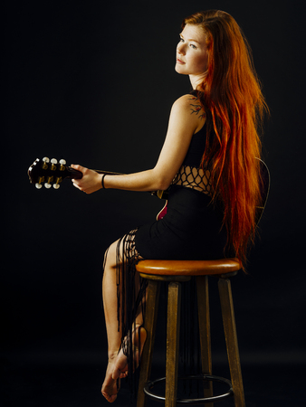Photo of a young beautiful redhead woman sitting playing an acoustic guitar.の写真素材