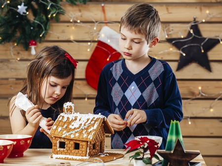 Photo of a young brother and sister decorating a gingerbread house at home just before Christmas.の写真素材