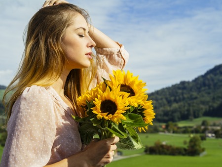 Photo of a happy young woman holding sunflowers in the sunshine.の写真素材