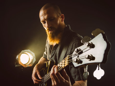 Photo of a bearded man playing bass guitar on stage in front of spotlights.
