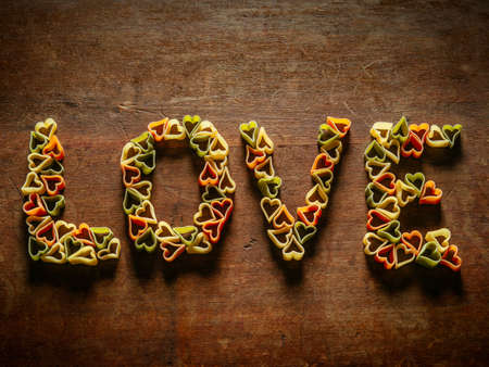 Wood table with heart-shaped pasta making the word love.の写真素材