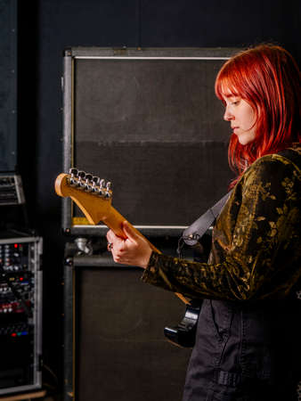 Young redhead woman playing electric guitar in front of large speaker cabinets.の写真素材