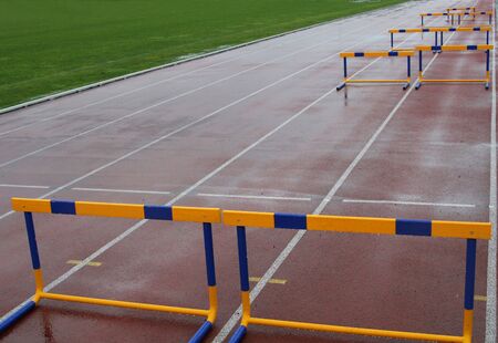 hurdles on a wet track field after heavy rain, with green wet grass showing on the left sideの写真素材