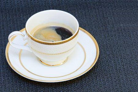 A fine china cup with high grade coffee in it, foam on top, the cup is standing alone on a plate on black bacgroundの写真素材