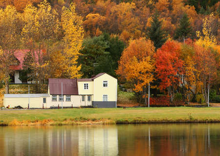 An old house in autumn, leaves in vivid color, reflecting in water.の写真素材
