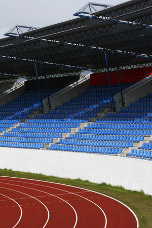 Sports stadium, curve in red tracks with white lines and blue seats in the audience box