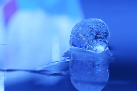 cold ice cube melting on blue background, copy space and reflection