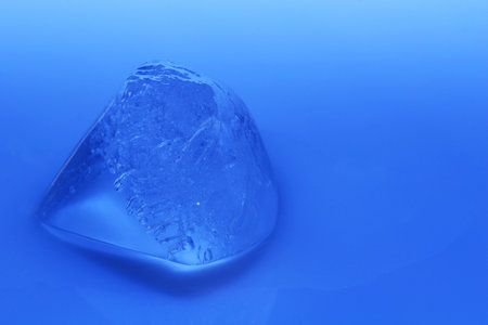 cold ice cube melting on blue background
