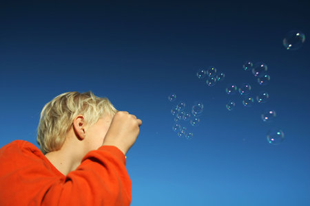 small boy blowing bubbles agains a deep blue sky