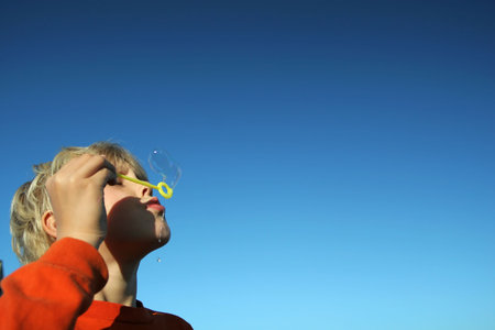small boy blowing bubbles agains a deep blue sky