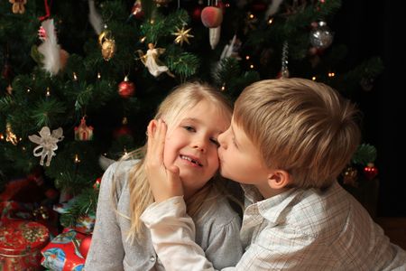 Young boy giving his little sister a kiss in front of a christmas tree with presents belowの写真素材