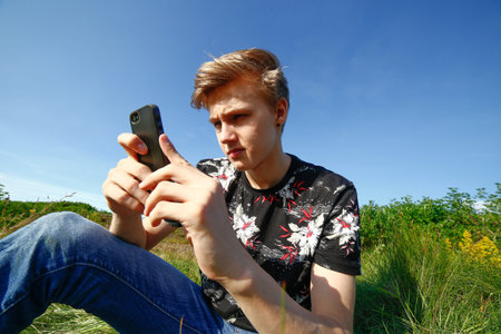 Teenager texting on his smartphone outside in summer