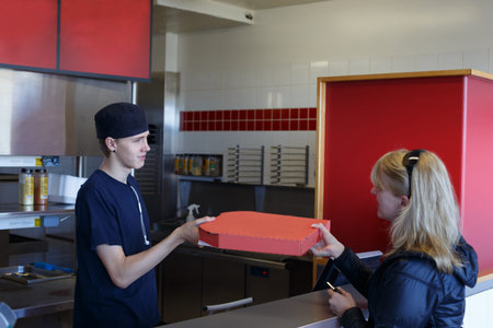 Young man handing over a pizza in a fast food restaurant