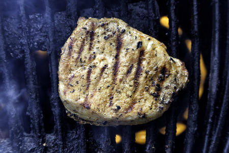 Single pork chop on a gas grill, flames visible below and smokeの写真素材