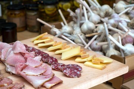 Cheese, sausages and smoked ham cut down ready to eat on a wooden board at a farmers marketの写真素材