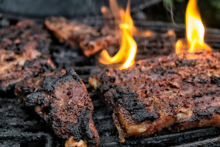pieces of meat on the barbecue, flames present arount them