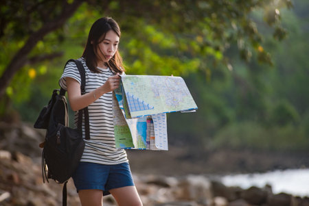 Young woman with backpack enjoying view on beach, looking a map.
