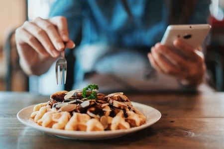 Hand of woman having breakfast and using on a mobile phone.の写真素材