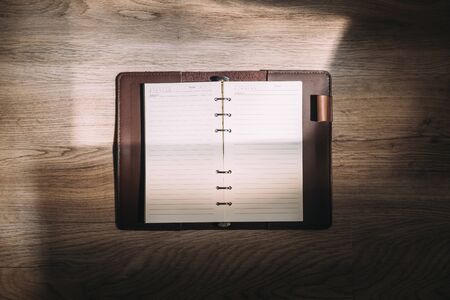 Top view of blank notebook on wooden desk in sunlight.の写真素材