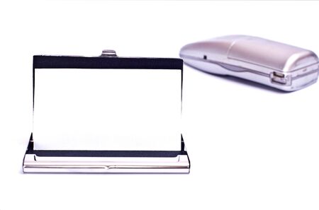 Business card in metal card holder and phone behind it isolated on whiteの写真素材