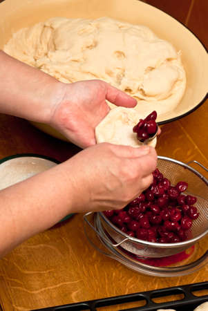 Female hands making small pies with cherry on a tableの写真素材