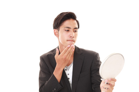 Asian man looking at his hair in mirrorの写真素材