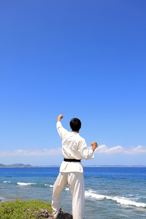 Young adult man with black belt practicing a Kata on the beach on a sunny day.の写真素材