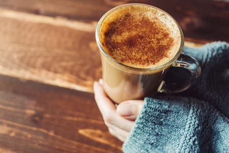 Female hands holding hot cappuccino with foam on wooden table in morning in the right, copy spaceの写真素材
