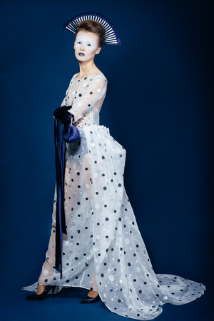 Full body shot of Japanese young woman in fashion elegant designers grey dress and blue velvet gloves on blue blackgroundの写真素材