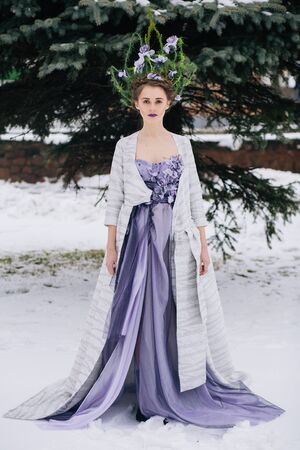 Outdoor full body shot of beautiful young woman in fashion elegant designer purple dress with crown in winterの写真素材