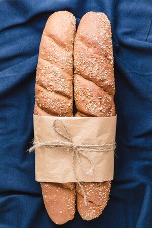 Two loafs of French baguette bread tied with paper and string on blue textile backgroundの写真素材