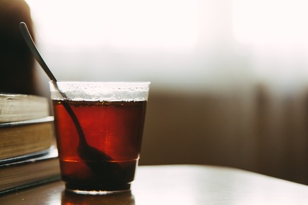 Cup of tea in transparent glass with spoon and stack of books on table at workplace in the morning, selective focus, copy spaceの写真素材