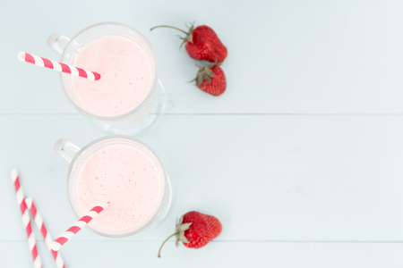 Two milk shakes with strawberries, ice-cream pink cocktail with straws on blue wooden table, copy space at right, top viewの写真素材