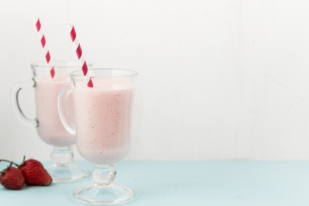 Two milk shakes with strawberries, ice-cream pink cocktail with straws on blue wooden table, copy space at right, top viewの写真素材