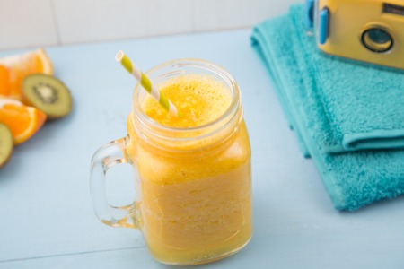 Juicy smoothie from orange, mango or pineapple, beachfront set with blue towels and camera, healthy life conceptの写真素材