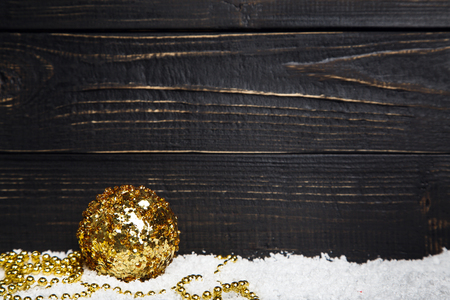 One golden Christmas ball on the snow with black rustic wooden background, copy space at the rightの写真素材