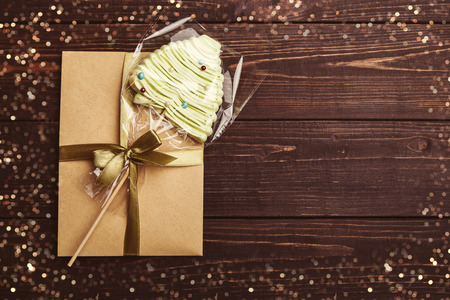 Craft envelope tied a green ribbon with meringue in the shape of Christmas tree on the brown rustic wooden background, New year gift concept, copy space at the rightの写真素材