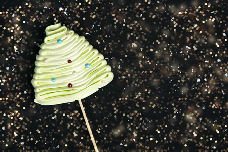 Green meringue in the shape of Christmas tree on the stick on the black background with snowflakes, sweetness for New Year holidays, copy space at the rightの写真素材