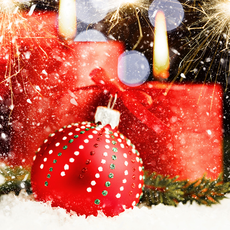 Red Christmas ball and burning candles on the snow with shining sparklers, bright colorful New Year backgroundの写真素材