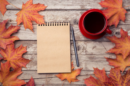 Autumn composition with workspace with blank notebook, pencil, red cup of coffee and beautiful red...