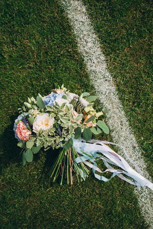 Beautiful elegant bridal bouquet from roses, hydrangeas, Brunias and Eucalyptus poplaraceous lying on a football lawn, wedding detail, copy spaceの写真素材