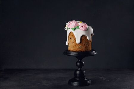 Easter cake with pink creamy roses on wooden black stand on dark grey textured background. Holiday concept. Easter inspiration. Copy spaceの写真素材
