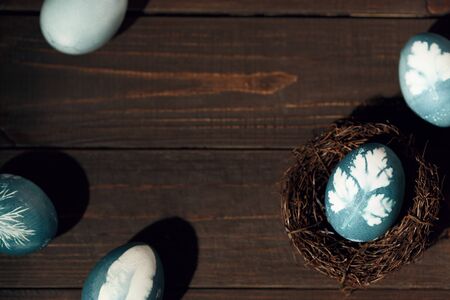 Painted blue eggs with printed picture of parsley in nest on wooden table. Easter decoration concept. Top view rustic backgroundの写真素材